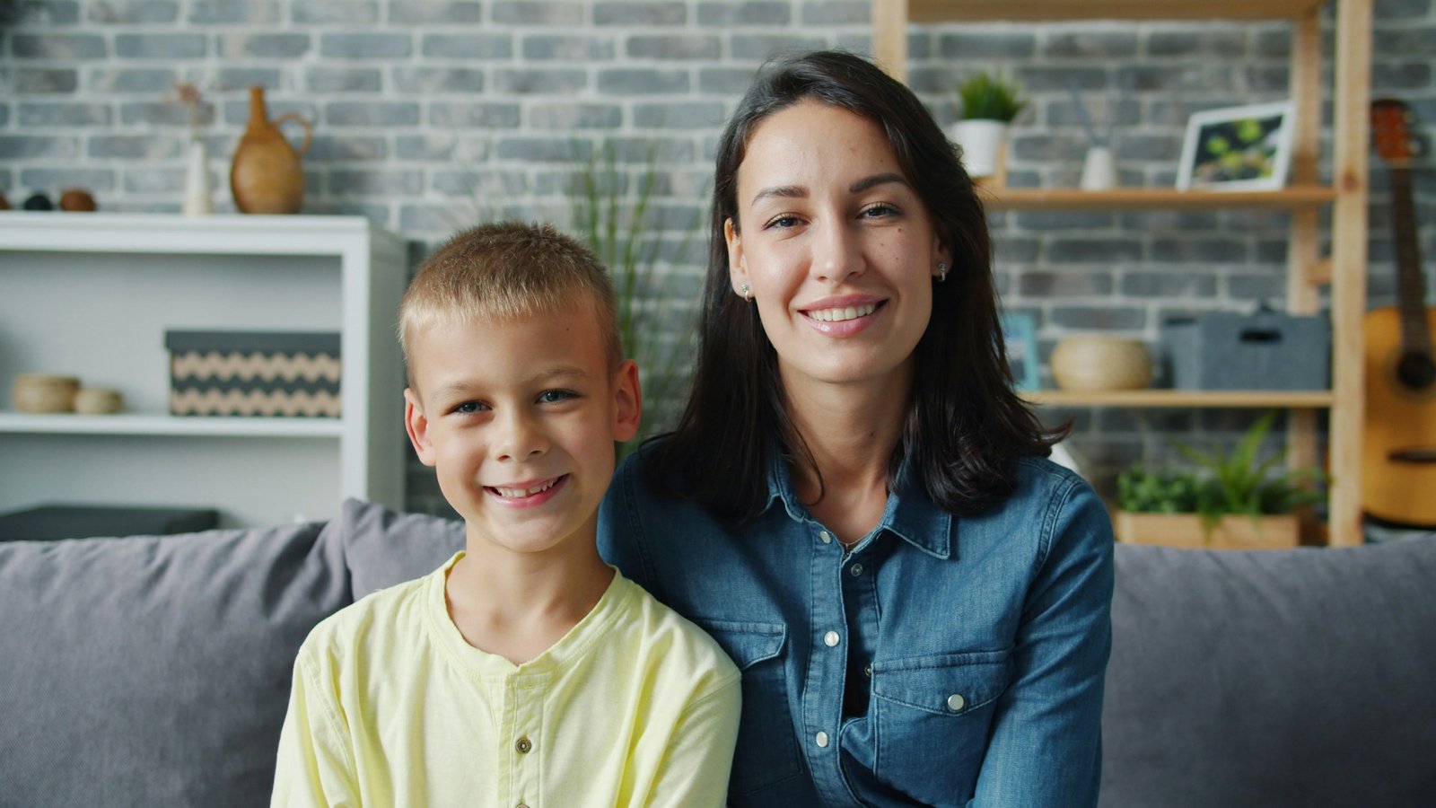A mother and young son smiling warmly at the camera together on a couch at home