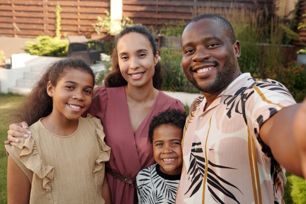 A smiling father, mother and two children posing close together in a sunny backyard